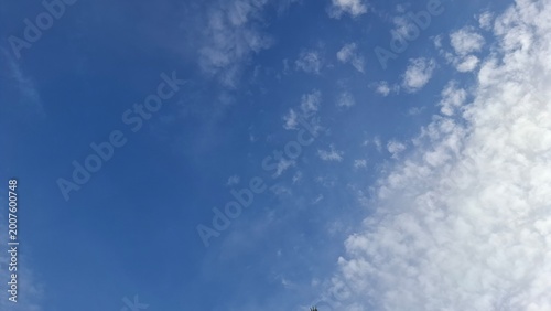 Deep vibrant blue sunny sky background lightly decorated with thin delicate scattered white cirrus clouds floating gracefully in the open air