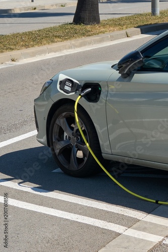 Konstfotografi A sleek gray hybrid vehicle is connected to a power supply at a public charging station in Catalonia, showcasing clean technology and eco-friendly transportation