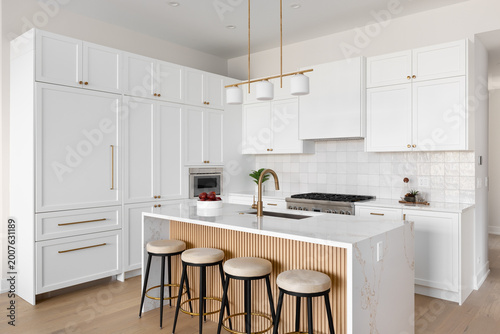 A kitchen detail with white cabinets and square tile backsplash, a waterfall marble countertop and wood slat panel front, and a gold light fixture, hardware, and faucet. No brands or labels.