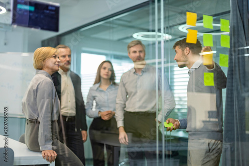Businesspeople talking in their diverse team during a brainstorming session with sticky notes on glass wall in a modern office
