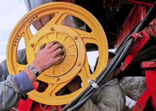 Workers repair a yellow wheel on a farm machine in a field during the afternoon