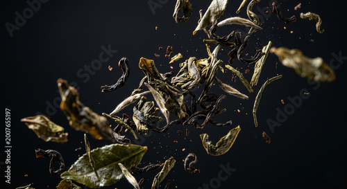 Dried tea leaves suspended in mid-air against a dark, moody background, captured in a dynamic, close-up shot