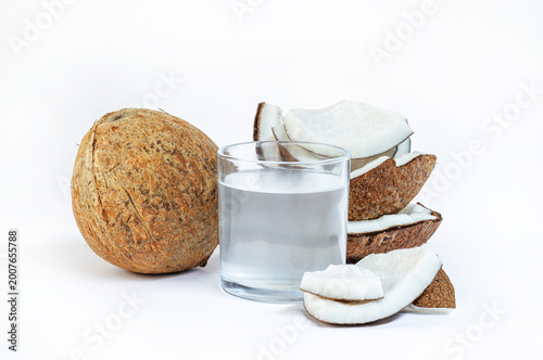 Fresh coconut water in a clear glass with whole and sliced coconuts on white background, minimal style, refreshing and healthy concept