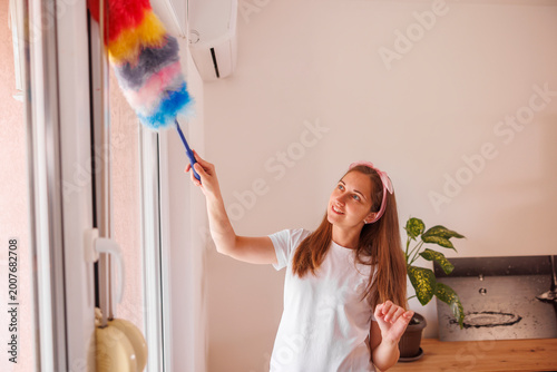 Woman using duster for taking the dust off the walls while deep cleaning the house