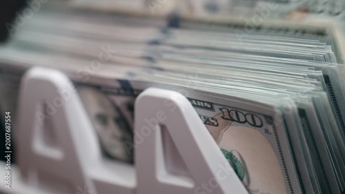 Close-up of 100 dollar banknotes being counted by an automatic money counting machine, crisp bills moving rapidly through device. Concept financial operations and cash processing technology.
