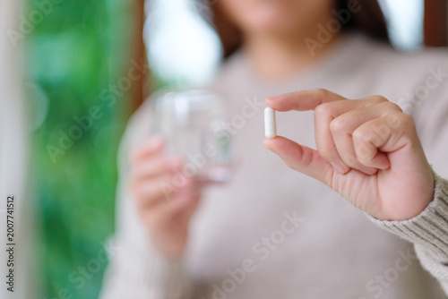 Closeup image of a woman holding a white pills and a glass of water