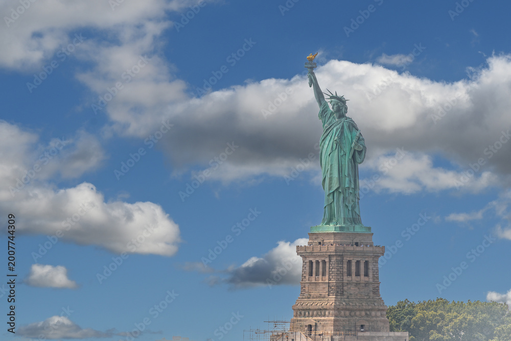 Fototapeta premium New york, usa august 16,2024. Iconic statue of liberty, an american landmark representing democracy and immigration, standing tall against a bright blue sky with clouds