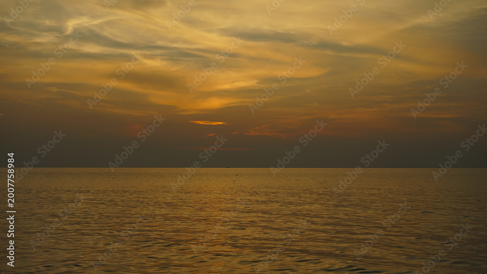 Obraz premium Golden sunset over the ocean with dramatic clouds reflecting warm tones across the water.