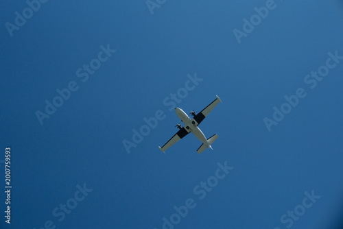 Tablou pe pânză Low Angle View of a Twin-Engine Propeller Plane Flying in Clear Blue Sky on Sunn