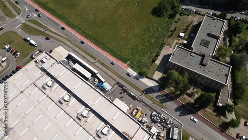 Aerial View of Industrial Park: An expansive industrial park seen from above, showcasing a large factory building with a loading dock, surrounding green spaces, and a busy road with vehicles.