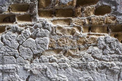 Tablou pe pânză Old brick wall showing peeling rough plaster texture