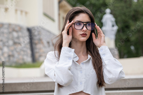 Fashion portrait of a young beautiful brunette in a white blouse and glasses