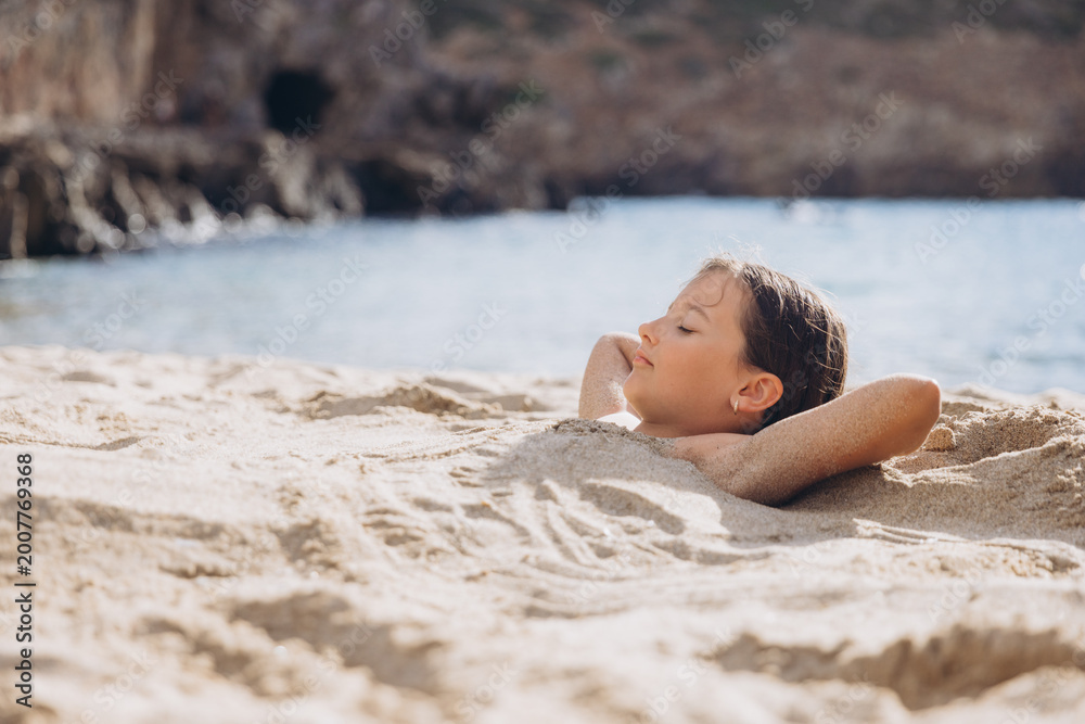 Fototapeta premium Young girl relaxing buried in sand at Cala Domestica beach, enjoying summer vacation in Sardinia, Italy