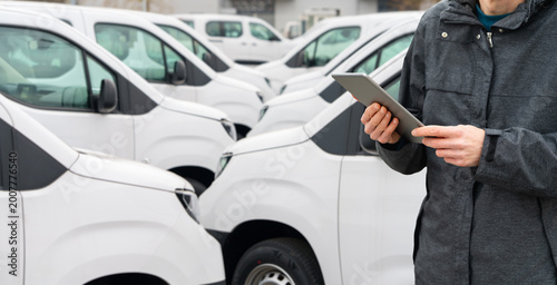 Photography Fleet manager with digital tablet supervising rows of white delivery vans