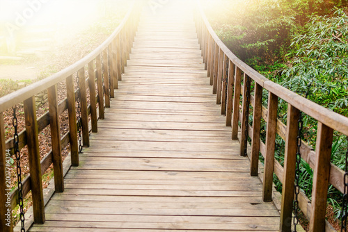 Empty wooden walkway with railings in a sunlit forest. Beautiful landscape with light at the end of the road. Way to success and freedom in nature during summer day.