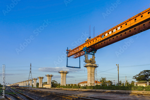 Construction of massive elevated railway viaduct using  gantry crane for girder installation. Elevated railway construction site with heavy machinery and concrete pillars for modernization transit.