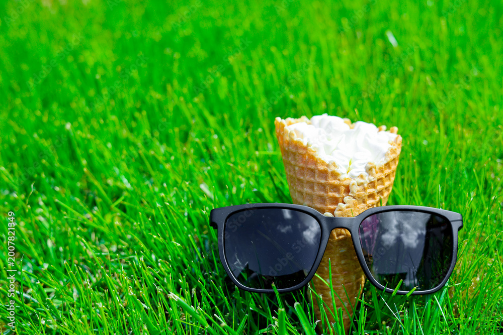 Naklejka premium Close up creamy ice cream and sunglasses in a serene lawn setting. Summer vacation concept. Ice cream on bright green grass background. 