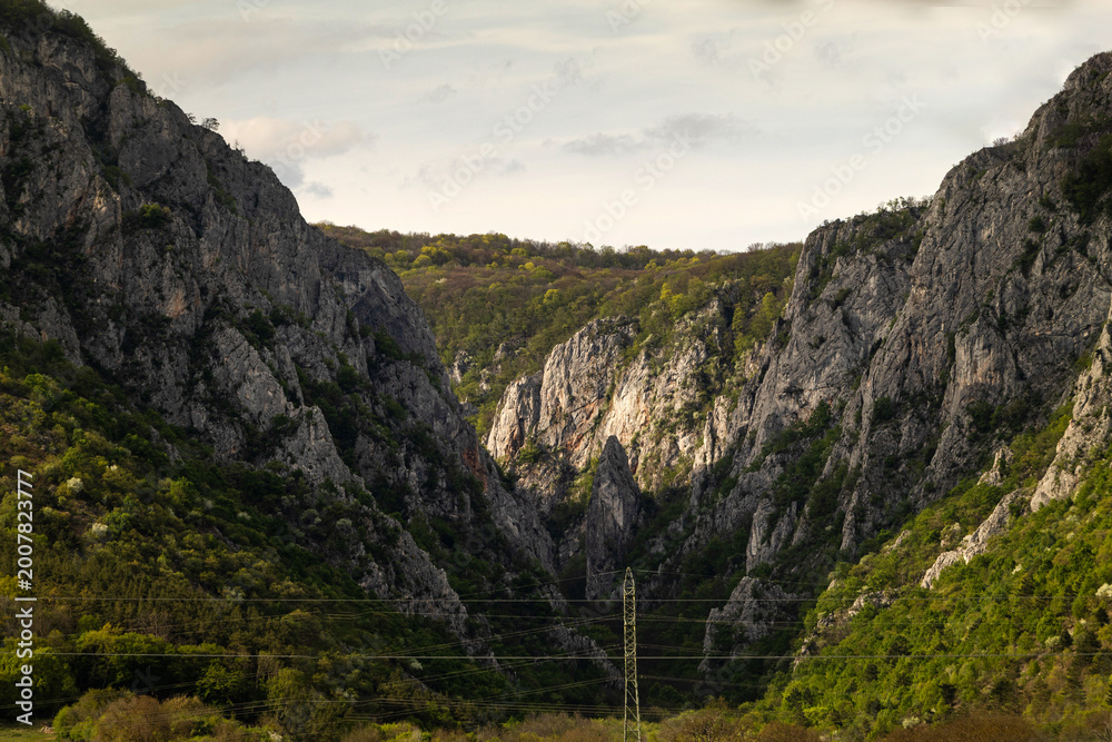 Fototapeta premium Mountains meet in a valley during late afternoon near a power line