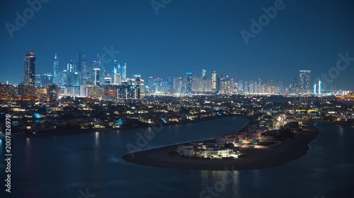 Stunning aerial view of Dubai Marina skyline at night with illuminated skyscrapers reflecting on calm waters, luxury Palm Jumeirah villas in foreground, deep blue twilight sky creating urban elegance.