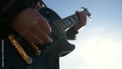 Close-up of hands playing electric guitar in sunlight, music and creativity concept