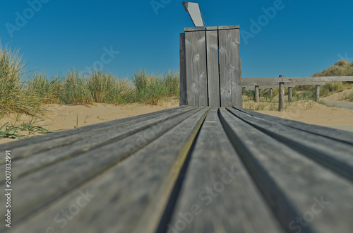 Tableau sur toile Low angle perspective of a wooden bench through sand dunes at the beach, Den Helder, Netherlands