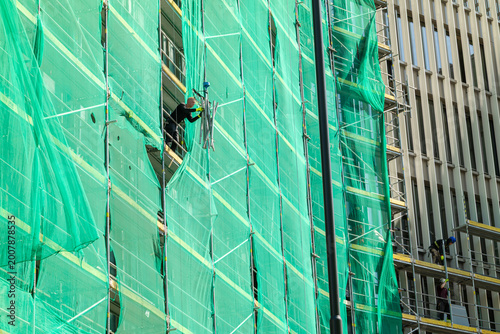 Canvas Print Workers on scaffolding at construction site covering building with green netting