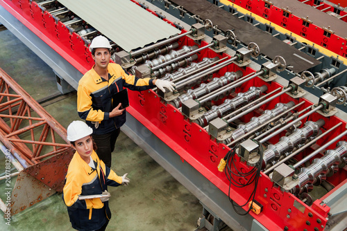 Photography Caucasian man uses tablet for metal sheet inspection during factory quality control assessment, conveying detailed process observation and professional focus in metal sheet factory