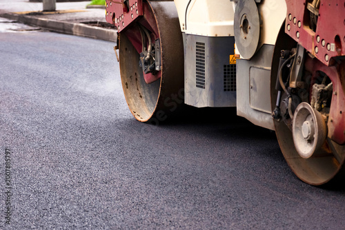 Heavy machinery is smoothing out fresh asphalt concrete on a city street. The road construction activity aims to create a safer and more durable surface for vehicles and pedestrians.