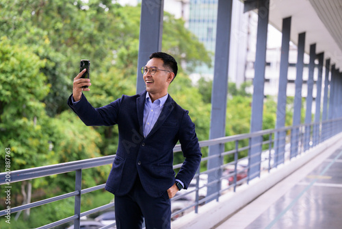 Smiling young businessman taking selfie on urban bridge