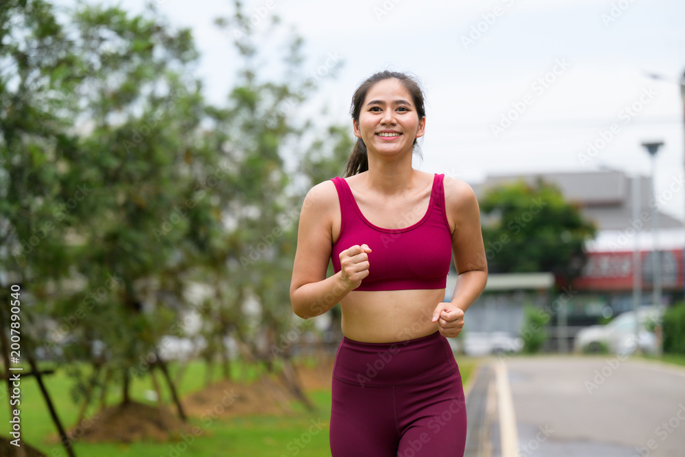 Fototapeta premium Young Asian woman jogging smiling outdoors