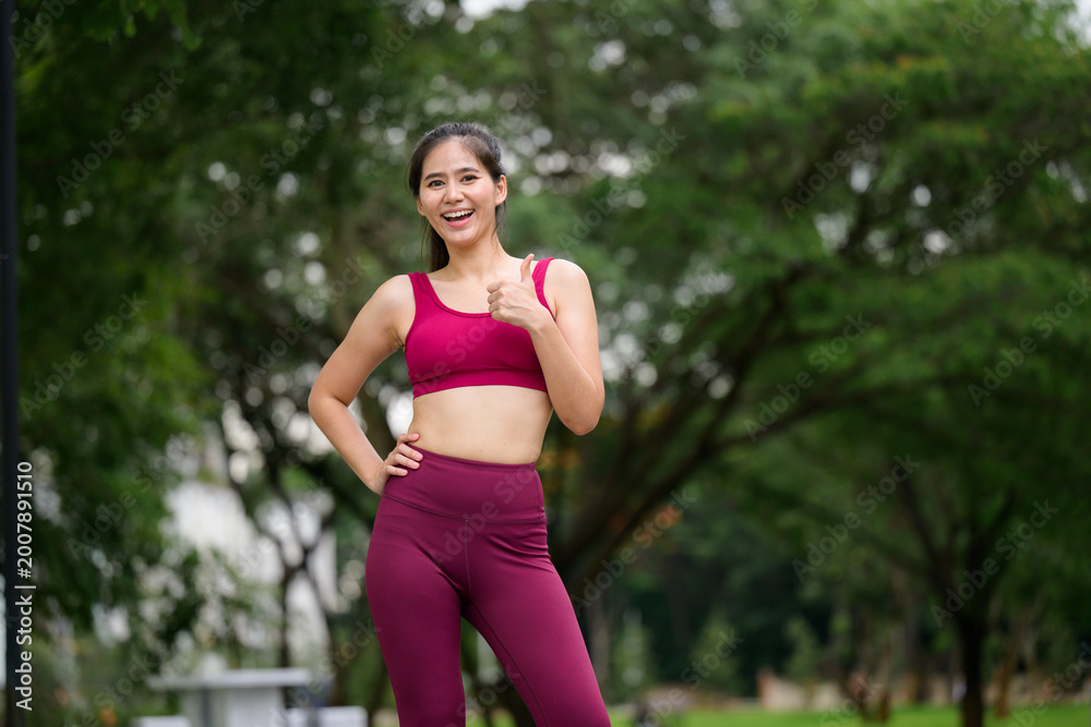 Fototapeta premium Young woman smiling giving thumbs up in park
