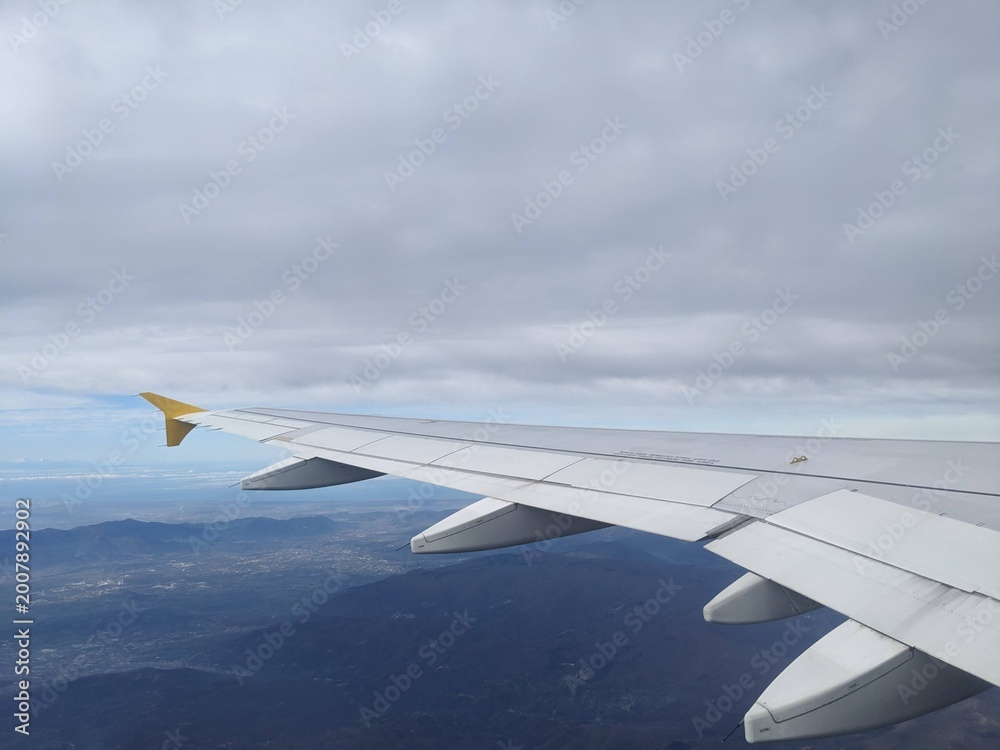 Obraz premium View from airplane window showing wing over mountains and clouds during flight