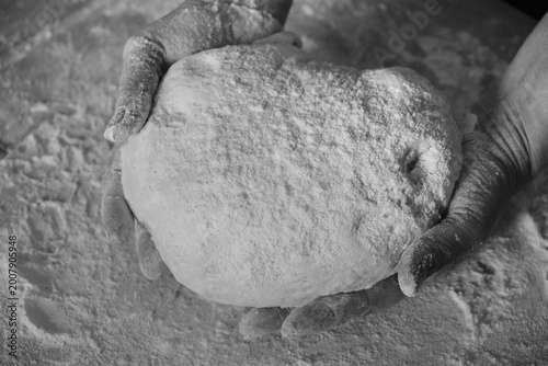 Skilled hands kneading artisanal dough with flour on the table, traditional gnocchi preparation, black and white photo.