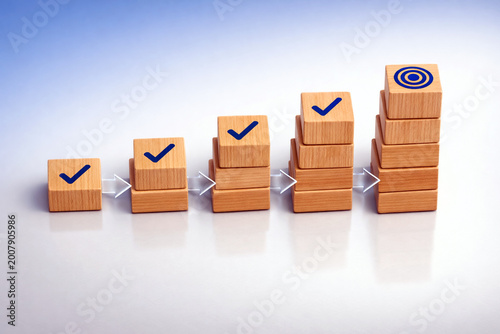 Wooden blocks arranged in a rising step formation display checkmarks alongside a central bullseye target icon to signify consistent progress and success in corporate growth. Business growth success
