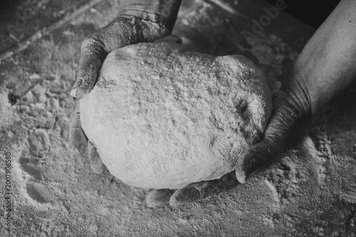 Skilled hands kneading artisanal dough with flour on the table, traditional gnocchi preparation, black and white photo.