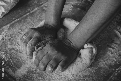 Skilled hands kneading artisanal dough with flour on the table, traditional gnocchi preparation, black and white photo.