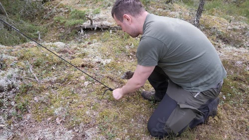 Man Kneeling in Forest Checking Cord on Mossy Ground