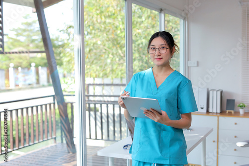 Fotografi Young female medical professional wearing scrubs, holding a stylus with a tablet