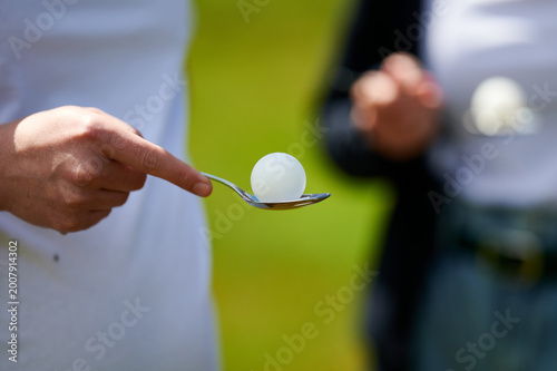Close up of a hand balancing a white table tennis ball on a metal spoon during an outdoor game, Poland, Europe.