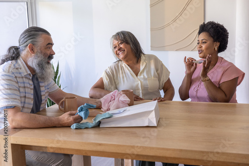 Diverse family chatting at home around wooden dining table with ceramic mugs and gift bag