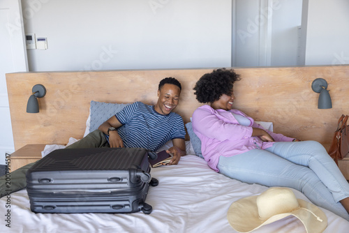 African American couple reclining in room in casual clothes, holding passport near suitcase and hat