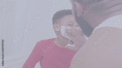 Father applying shaving foam to son in bathroom, reaching to teach playful hygiene routine