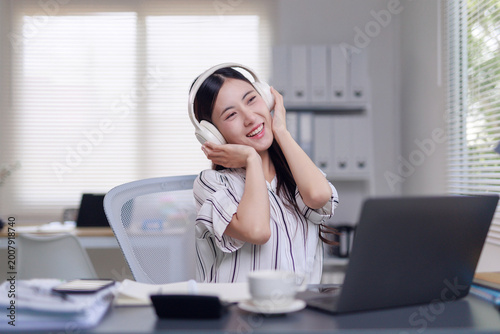Young woman smiling, listening to music and relaxing with wireless headphones in a modern office workplace