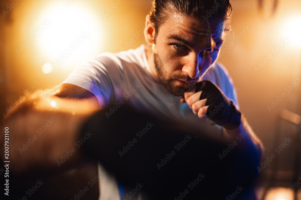 Fototapeta premium Male athlete with determined expression training hard, sweating during intense boxing workout, showing focus and power