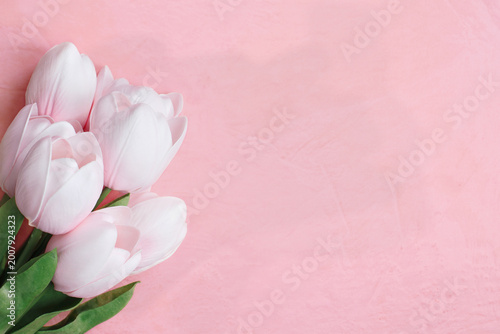 Beautiful soft pink tulips over pink textured homemade paper with copy space. Flatlay image for Mother's Day or other special occasions. 