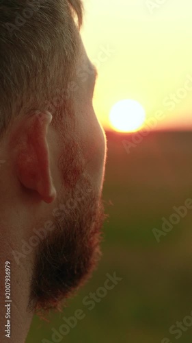 Free man pensively looks at setting sun. Tourist gazes into distance in nature. Portrait of man, close-up face. Happy man prays outdoors, sunrise, religion. Human journey. Man enjoys beautiful nature