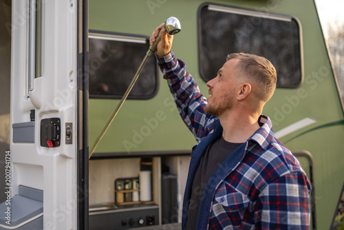 Side profile of a man looking at an outdoor shower head on a green travel traile