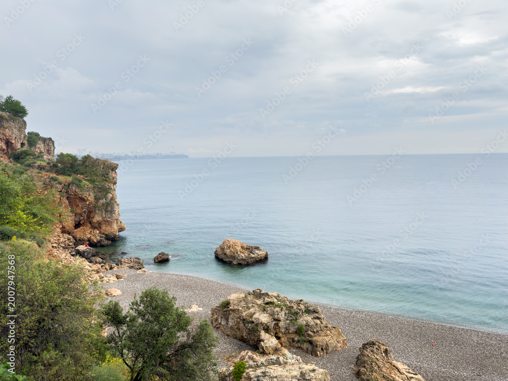 Naklejka premium Small rocky cove beach with cliffs on rainy cloudy day