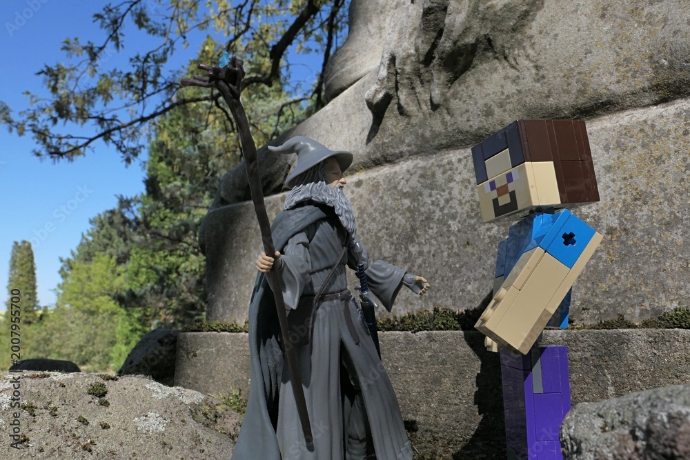 Naklejka premium Minecraft figure of main character Steve meets action figure of wizard Gandalf from novel Hobit and Lord Of The Rings by J.R.R.Tolkien under ancient stone pedestal of lion statue, spring sunshine. 