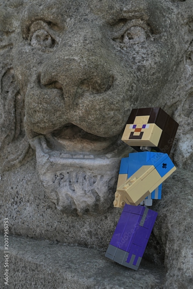 Naklejka premium Action figure of main Minecraft Character Steve standing at open mouth of a giant lion statue in park.